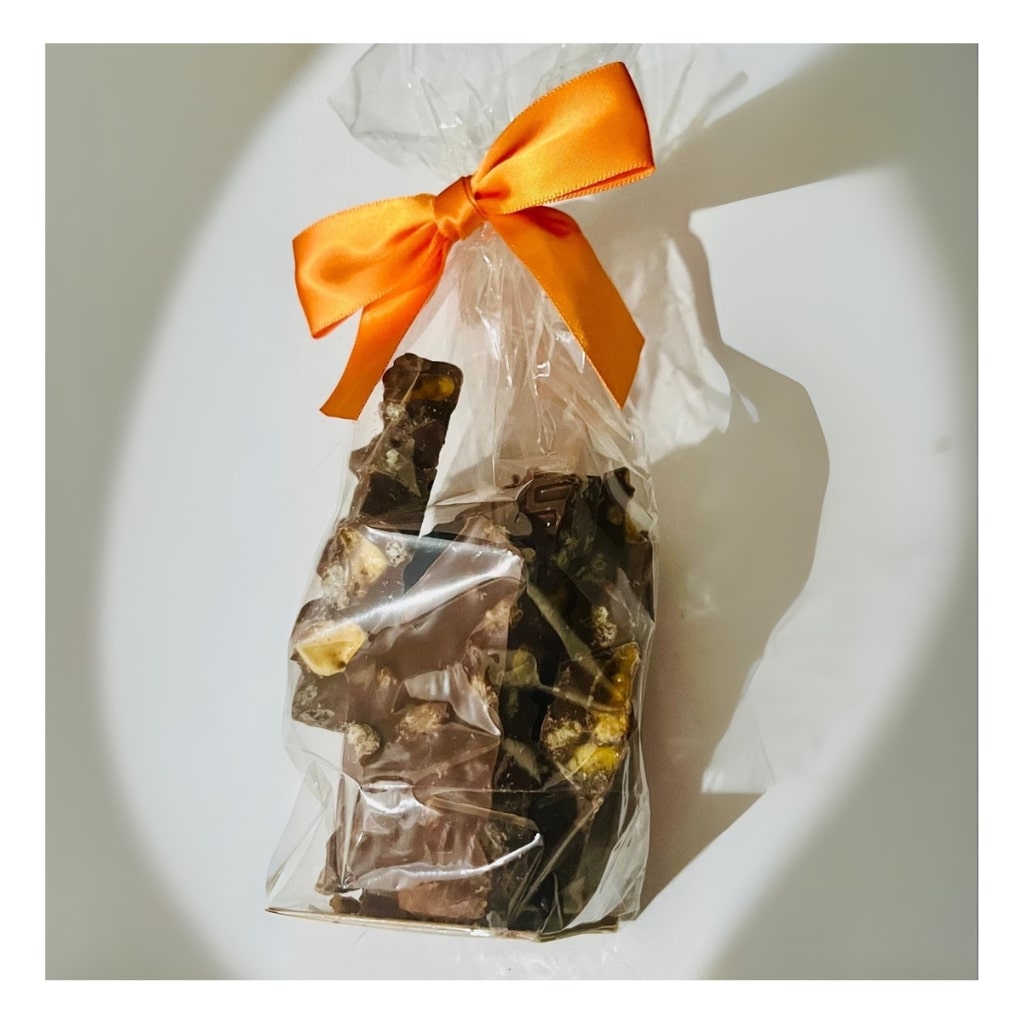 Clear plastic bag with honeycomb krisp chocolate pieces and an orange ribbon on a white background